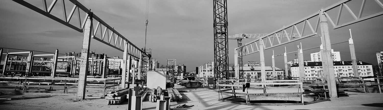 Nave industrial en construcción con pilares y cerchas prefabricados y una grúa torre